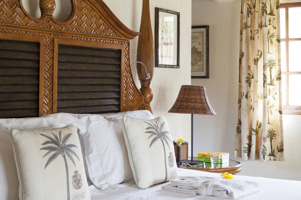 A neatly made bed with a wooden headboard, a ceiling fan, and a window with curtains.