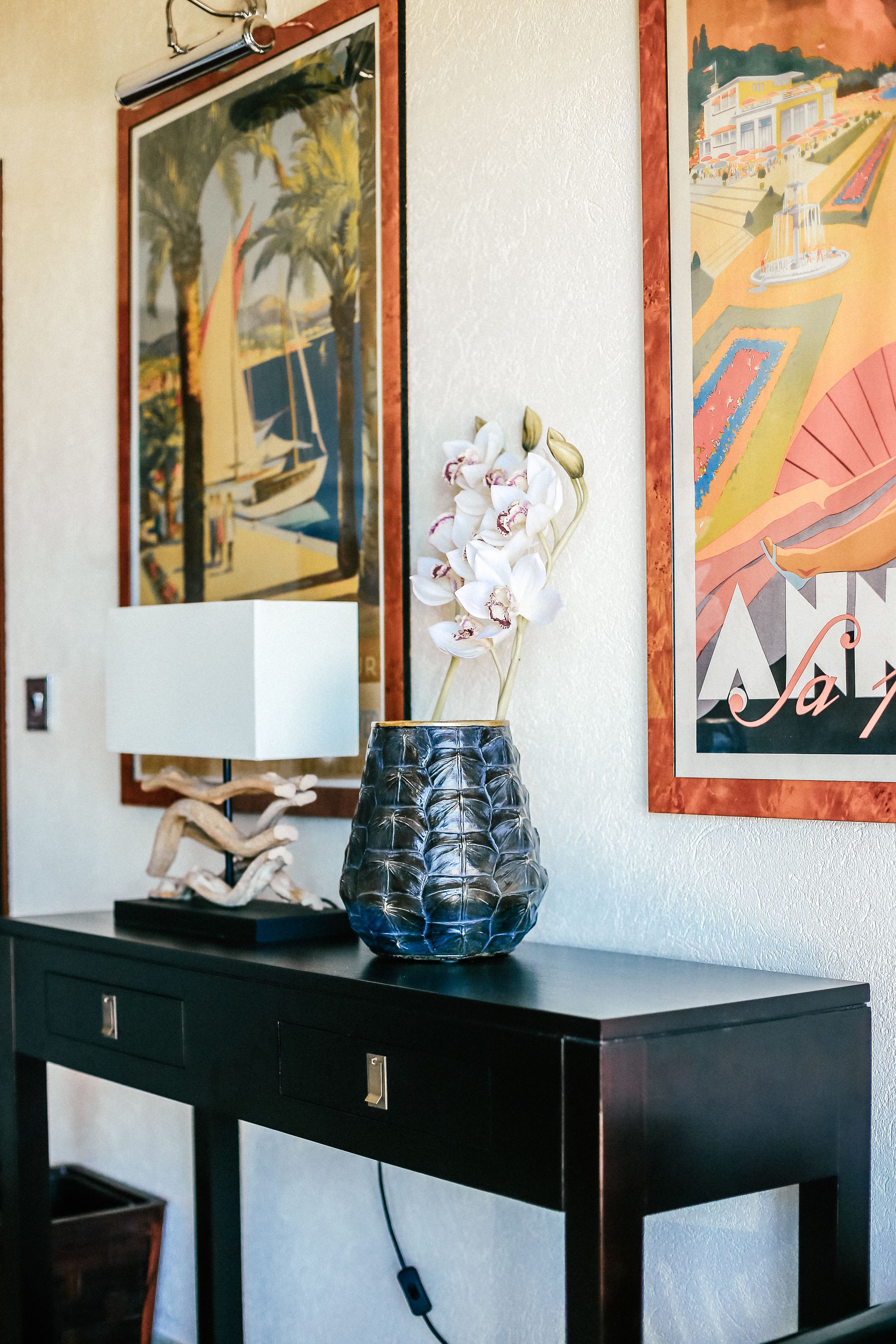 A desk with a vase of orchids, a framed painting, and a lamp.