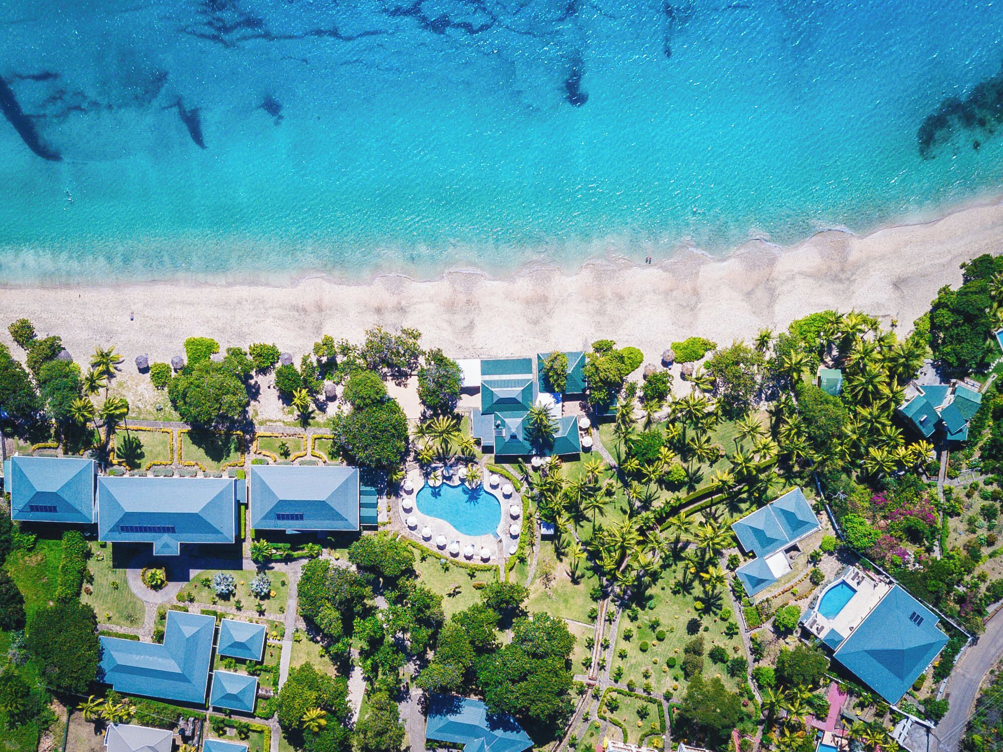 An aerial view of a resort with multiple buildings, a swimming pool, and a beach.