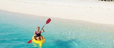 A person kayaking on clear turquoise water near a white sandy beach with a small island in the distance.