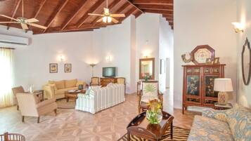 A spacious living room with a high ceiling, wooden beams, a television, and various seating options.