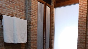 Une salle de bain avec un mur en briques, des toilettes blanches et une porte coulissante en verre donnant sur l’espace de la douche.