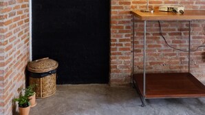 Une pièce avec un mur en briques, une porte noire, une table en bois avec une lampe et deux plantes en pot.