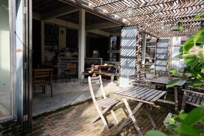 An outdoor seating area with wooden tables and chairs, a brick floor, and a sheltered section with a patterned ceiling. - Samatha Bed & Breakfast (Koh Tao)