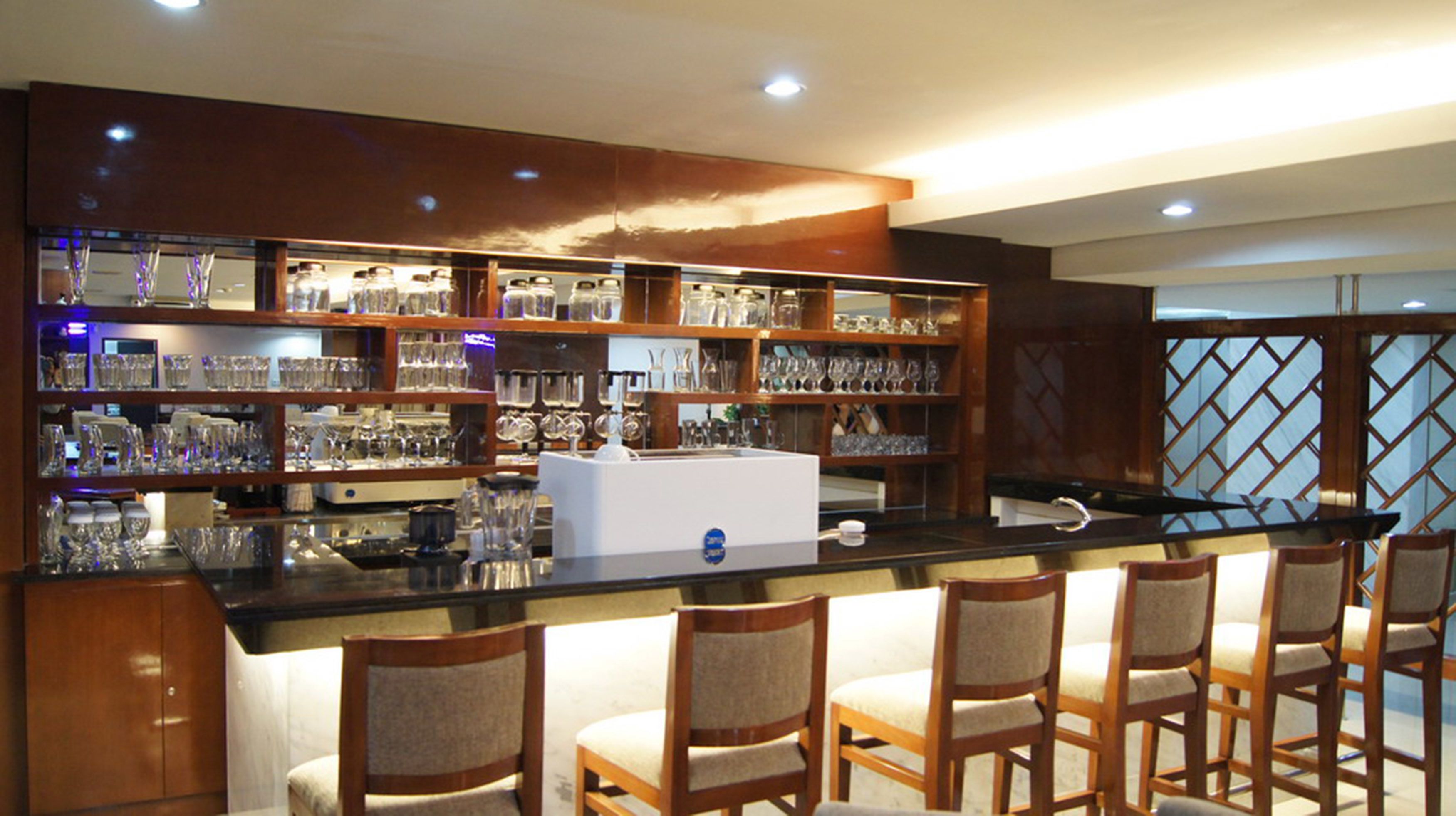 A bar area with wooden chairs, shelves of glassware, and a white bar counter.