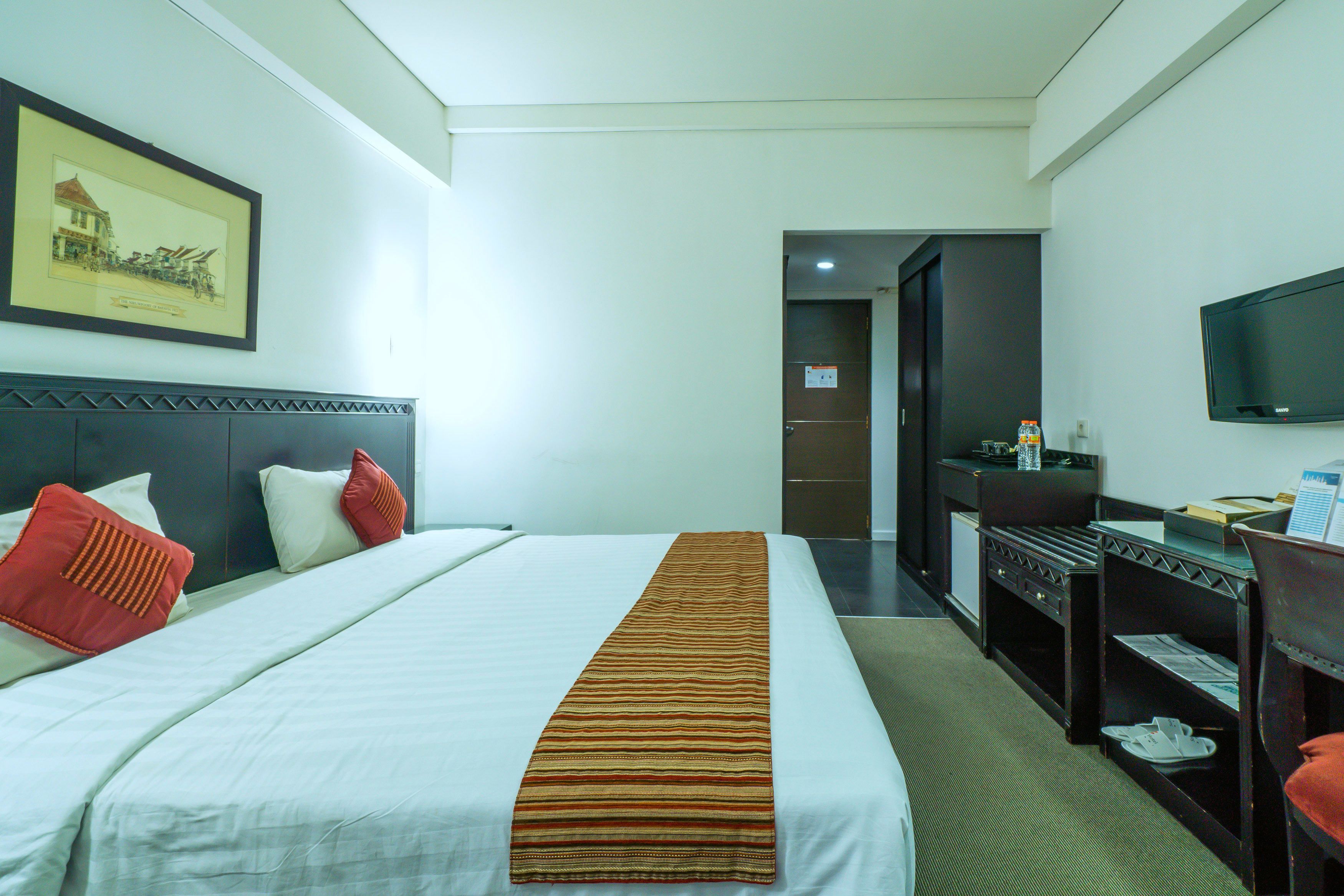 Ein Hotelzimmer mit Bett, Schreibtisch, Fernseher und einem gerahmten Bild an der Wand.
