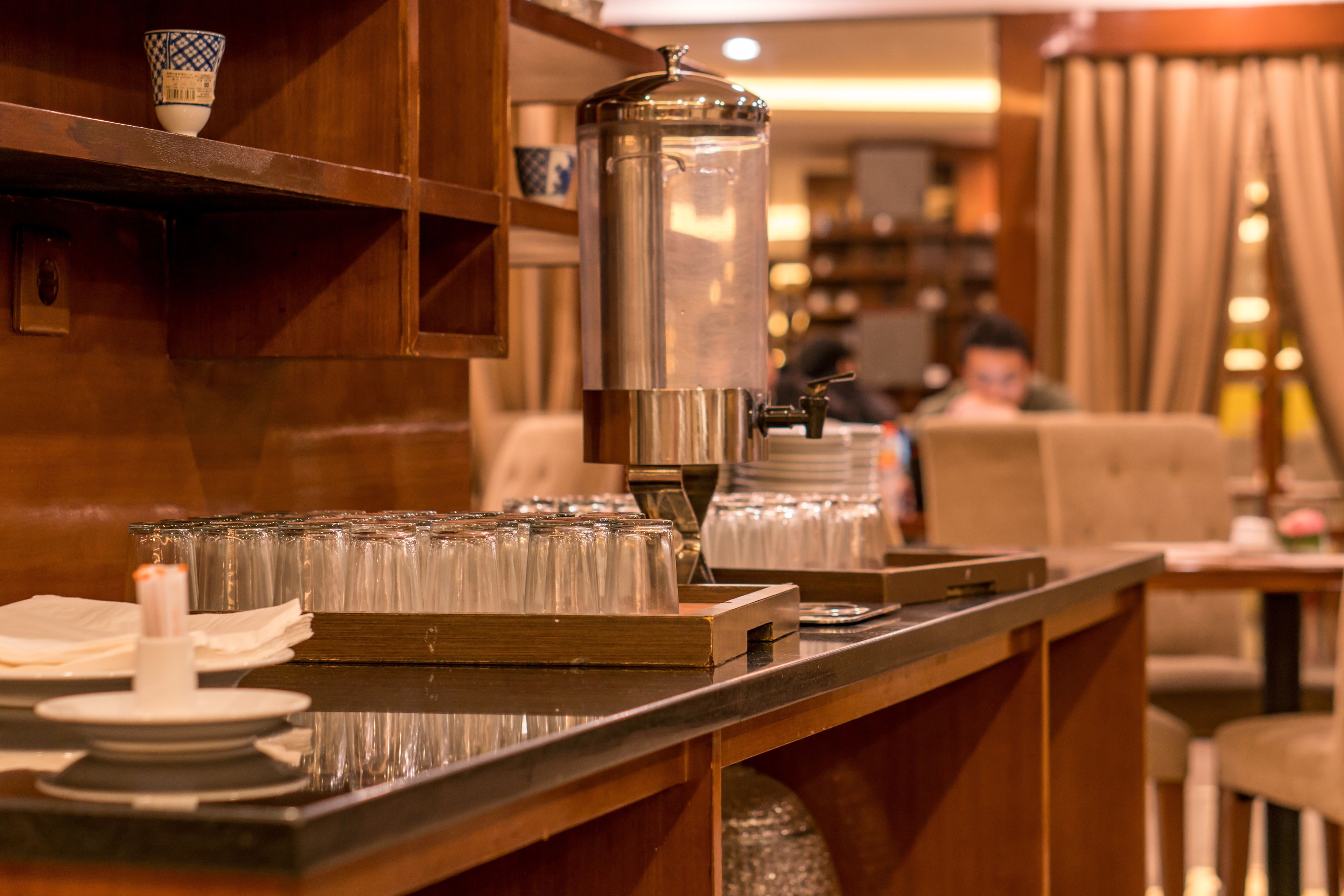 A coffee station with a coffee dispenser, cups, and a candle on a wooden counter.