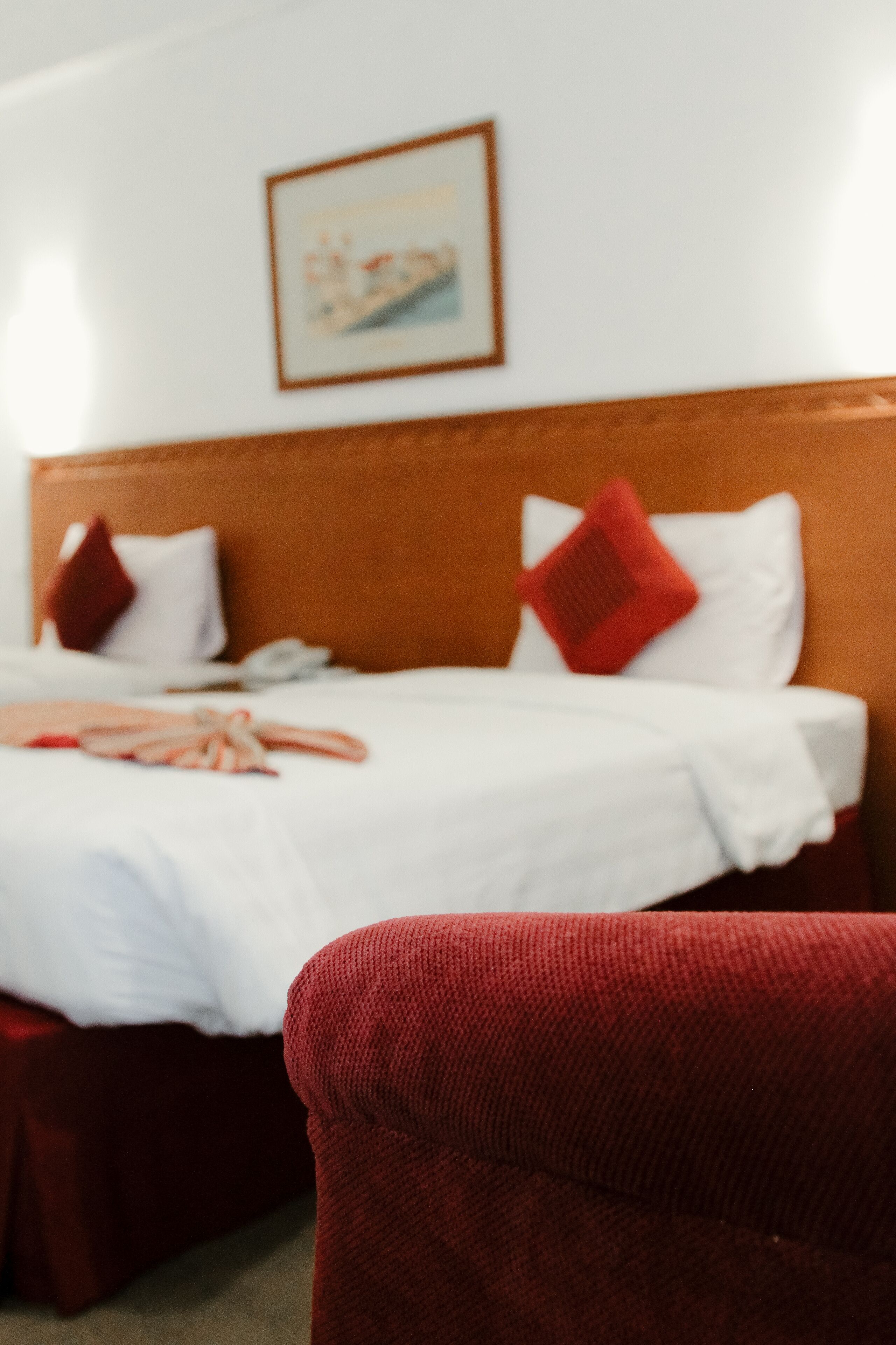Una cama con sábanas blancas, cabecera de madera y almohadas rojas.