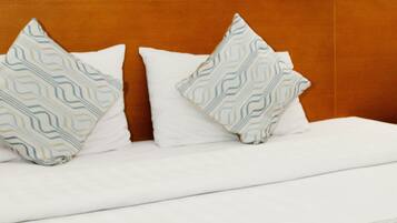 Una cama bien tendida con almohadas estampadas y un edredón doblado, un cuadro en la pared y un cabecero de madera.