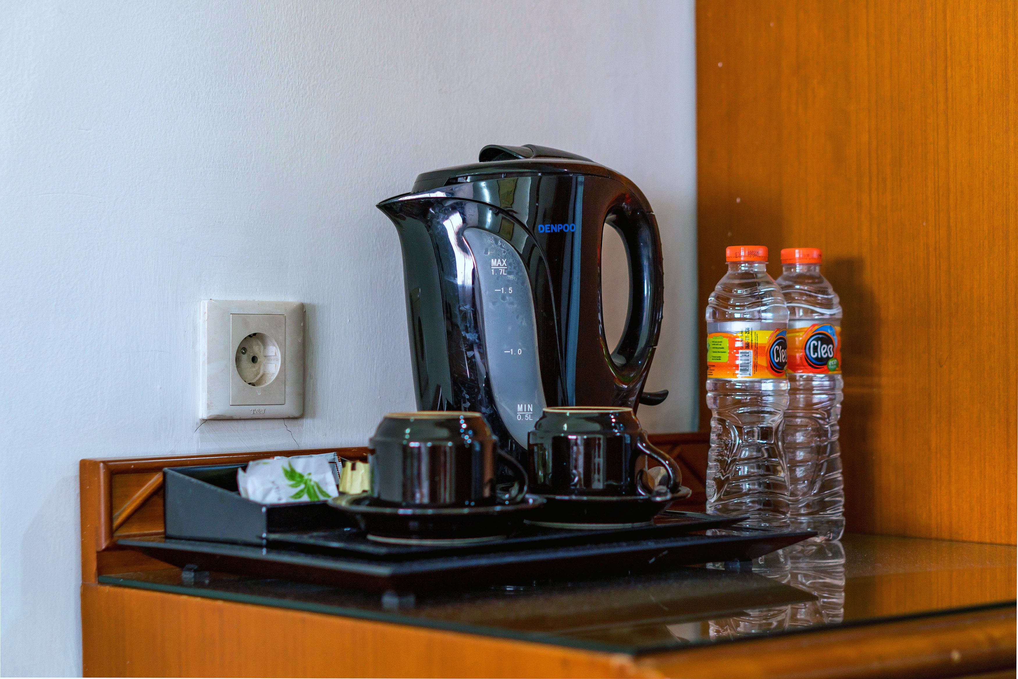 A coffee maker, two cups, and two bottles of water on a counter.