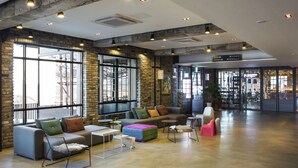 Un hall amplio con diseño industrial moderno, que cuenta con un gran espacio de estar con sofás y sillones, ventanas grandes y una escalera visible que lleva a otras zonas.