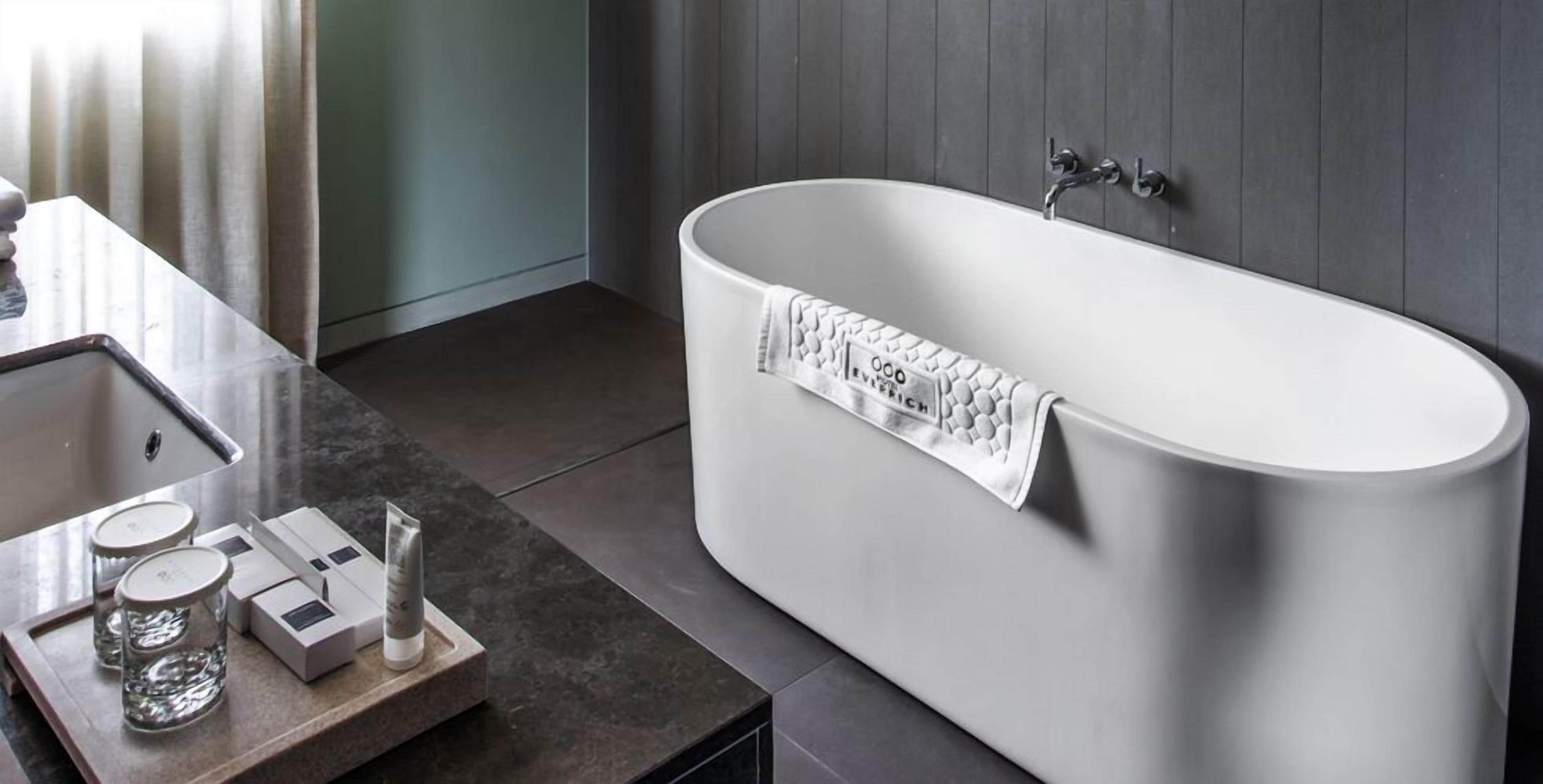 A modern bathroom with a freestanding bathtub, a vanity with a sink, and a tray with glassware and toiletries.