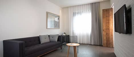 En moderne stue med en mørk sofa, et lille træbord og et stort vindue med gardiner.
