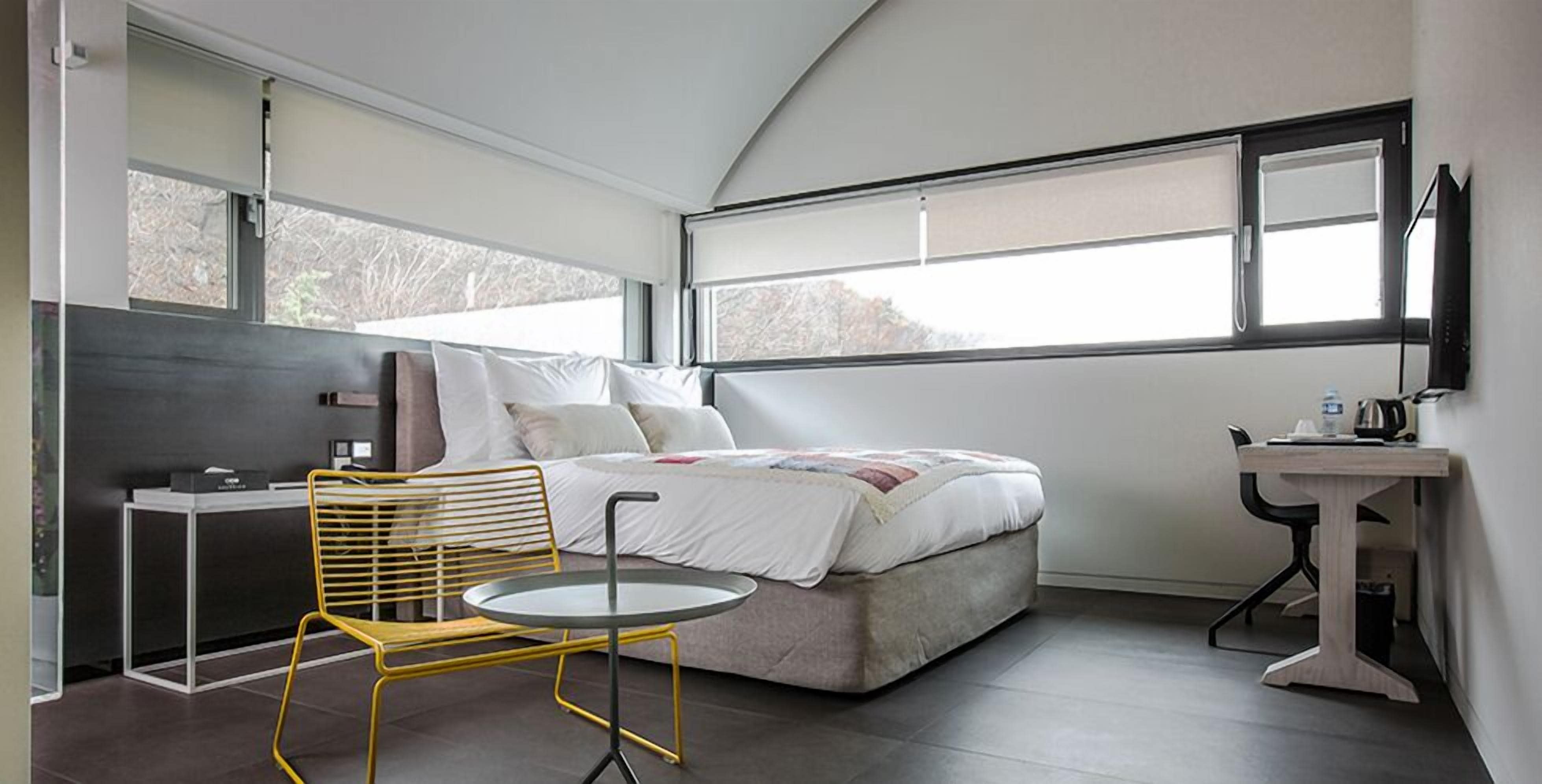 Un dormitorio moderno con una cama, una mesita, una silla y un escritorio.