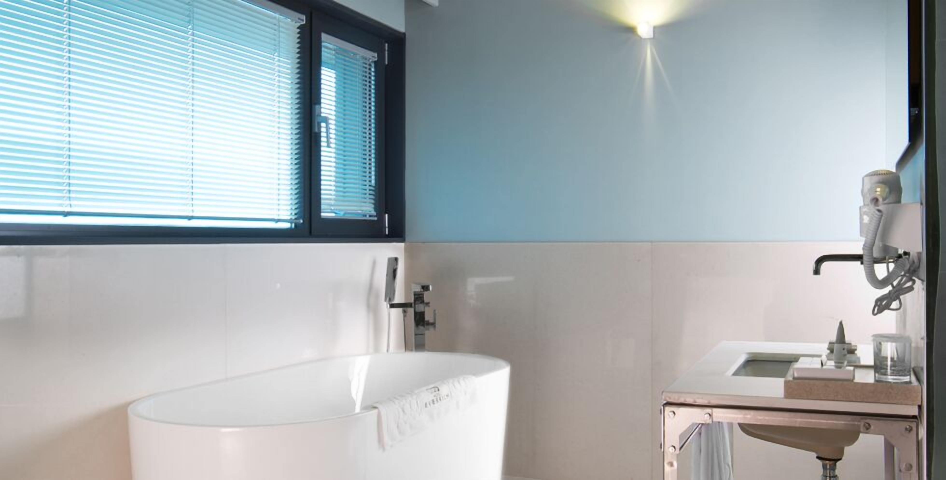A modern bathroom with a freestanding bathtub, a sink with a mirror, and a window with blinds.