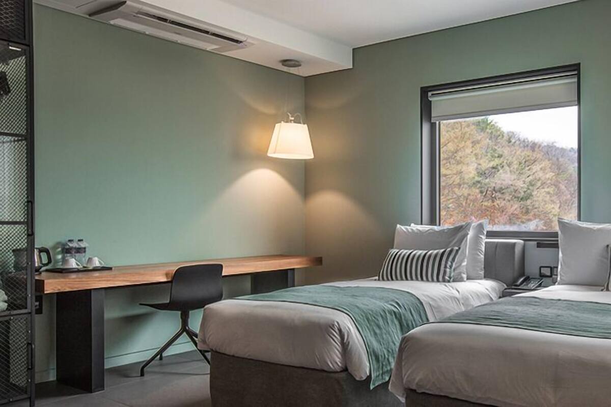 A modern hotel room with a large bed, a desk, and a window with a view of trees.