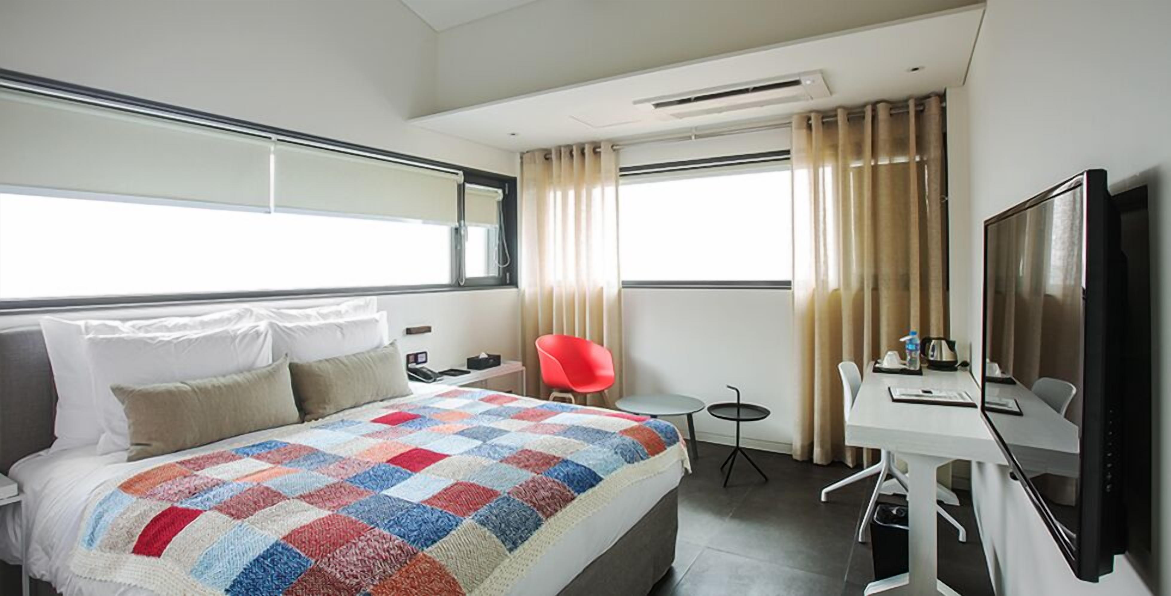 A hotel room with a bed, a desk, a chair, a TV, and a window with curtains.