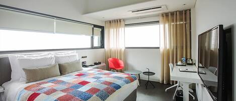 A hotel room with a bed, a desk, a chair, a TV, and a window with curtains.