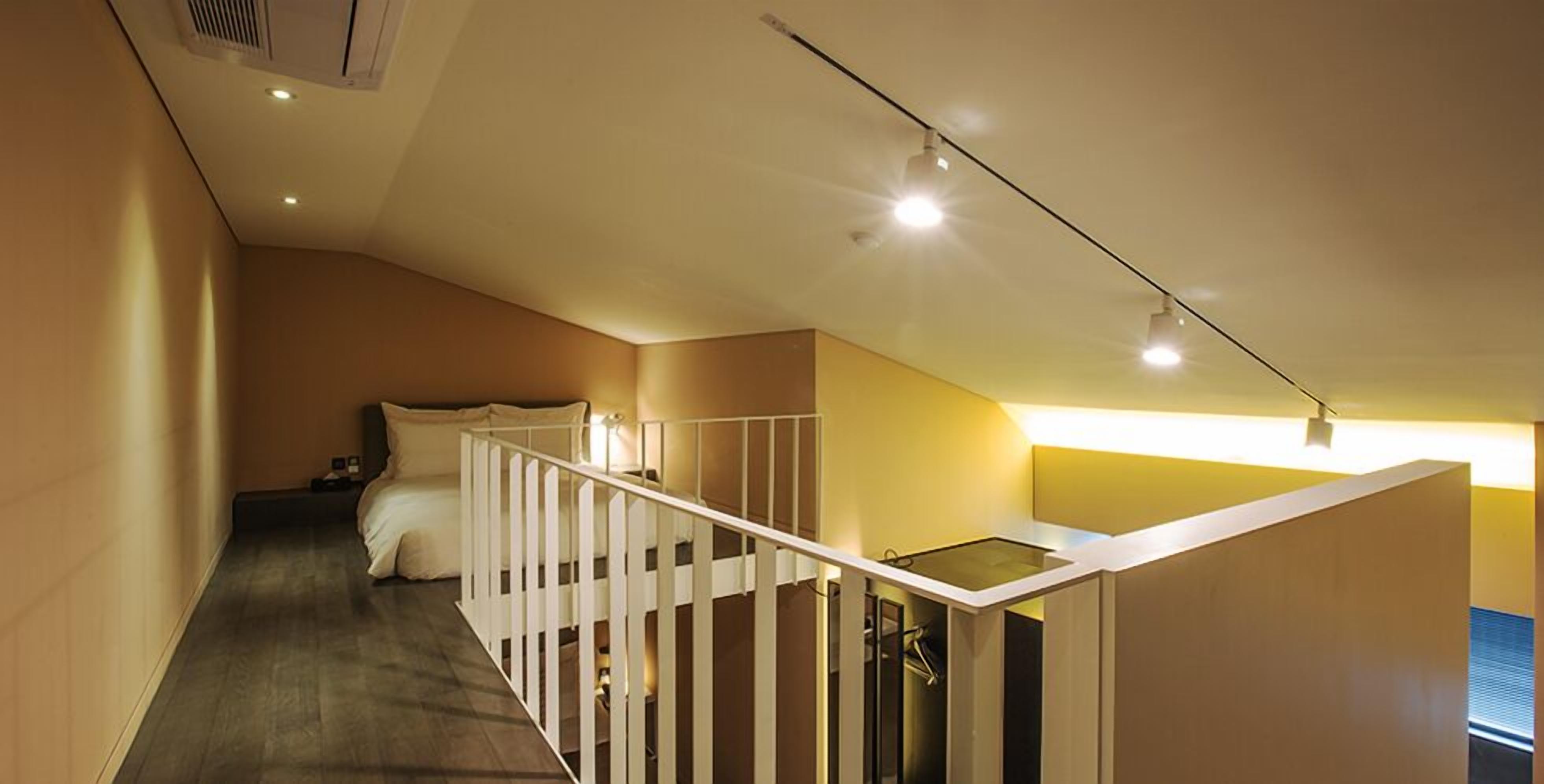 A modern hotel room with a wooden floor, a bed with white linens, a white railing, and a skylight.
