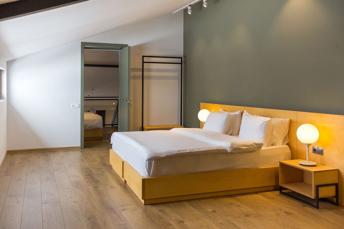 Un dormitorio moderno con cama de madera, lámparas de noche y vistas a una habitación contigua.