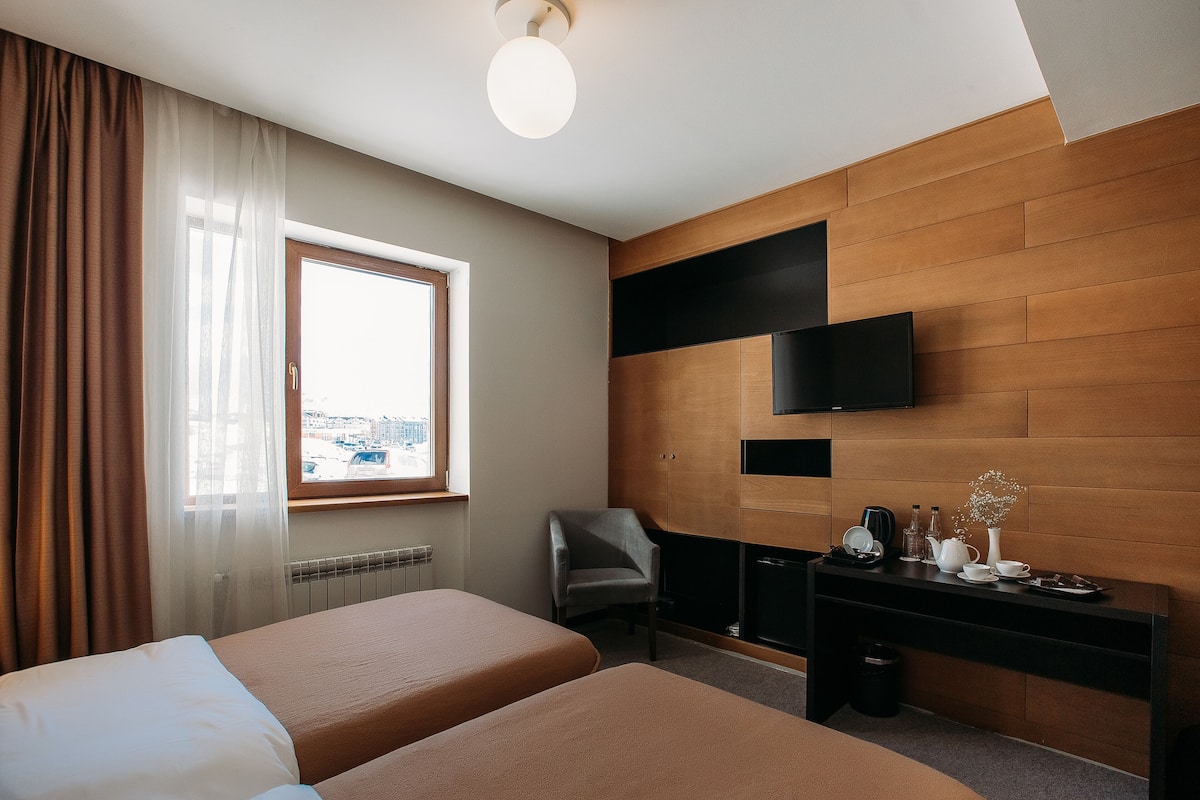 Habitación de hotel con dos camas, un escritorio, un televisor de pantalla plana, una silla y una ventana con cortinas.