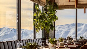 Un restaurante con vistas a la montaña, mesas de madera y plantas colgantes.
