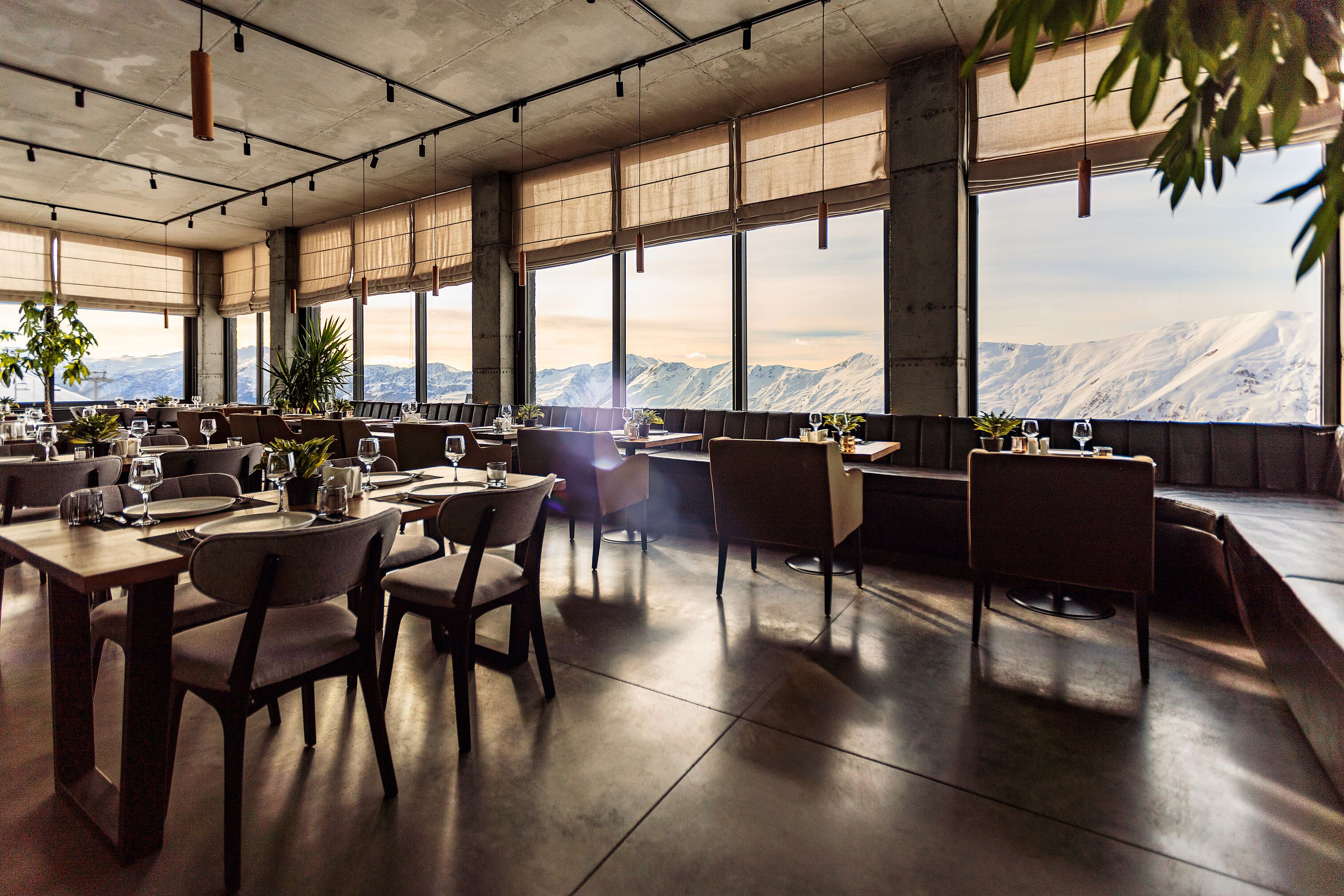 Un restaurante con vistas a montañas nevadas, ventanas amplias y mobiliario moderno.