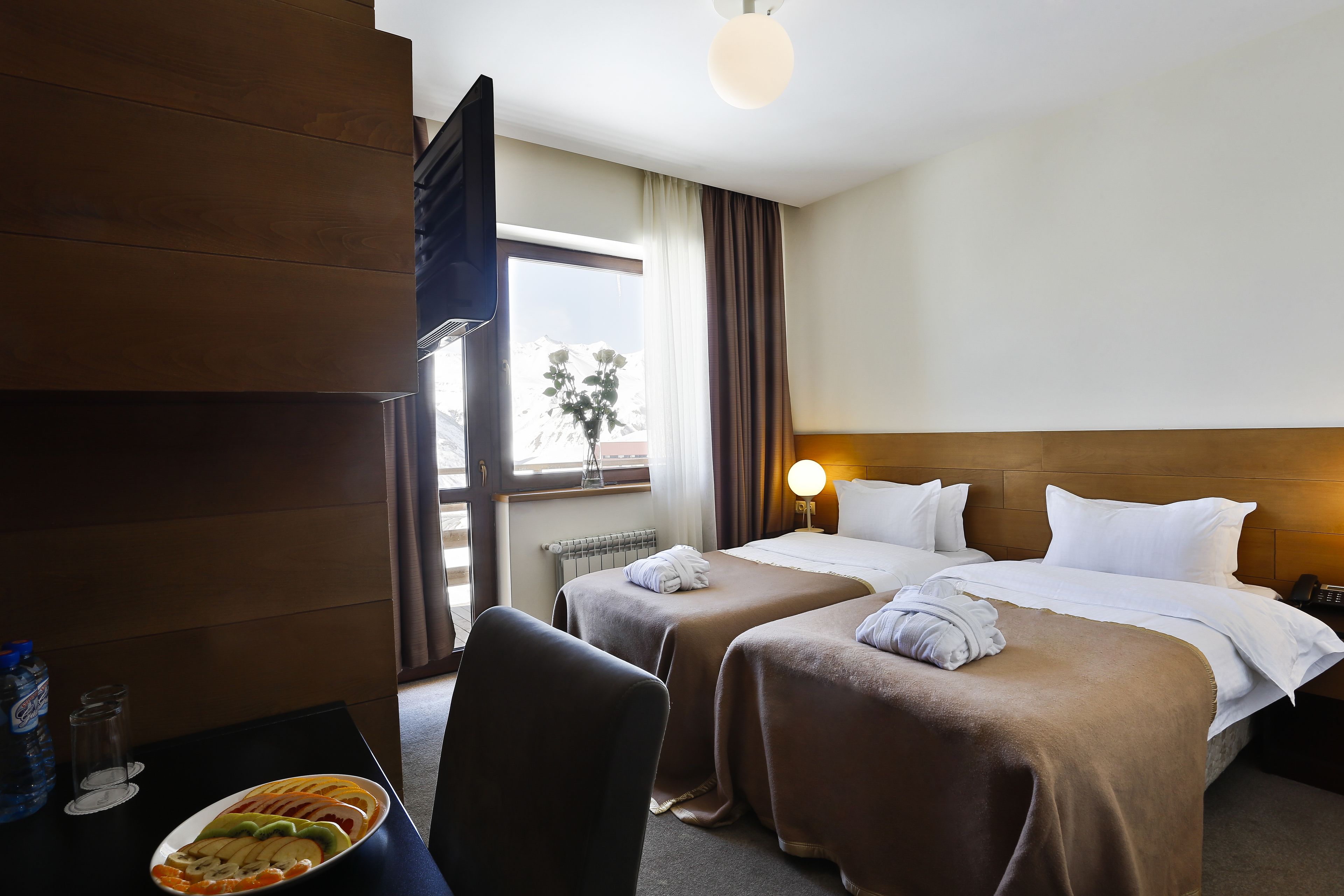 A hotel room with two beds, a desk with a laptop, a chair, and a fruit bowl.