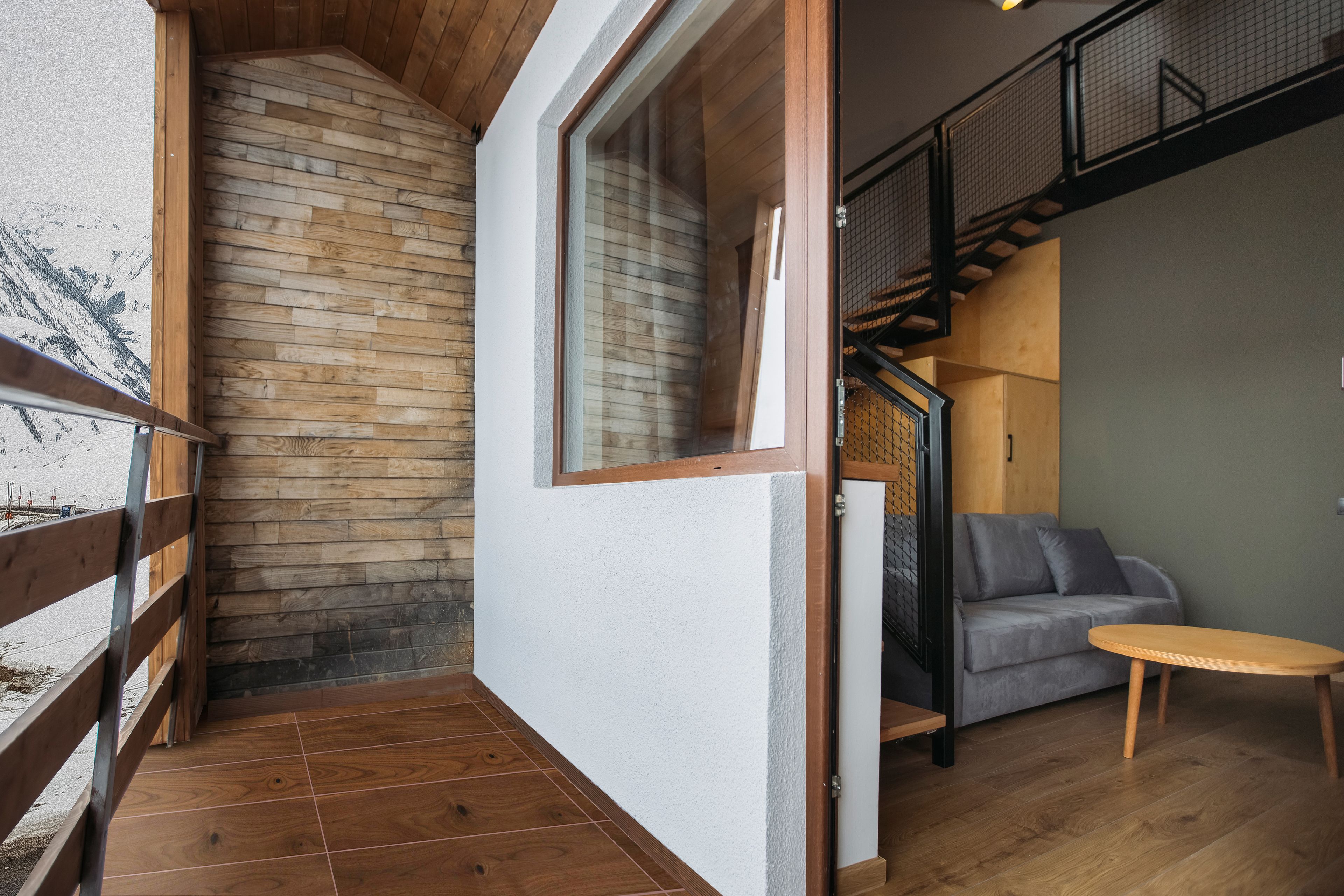 A modern interior with a wooden staircase, a gray sofa, and a wooden table.