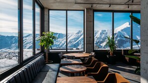 Un interior moderno con grandes ventanales que ofrecen vistas a la montaña. Varias mesas y sillas de madera dispuestas para comer o conversar.