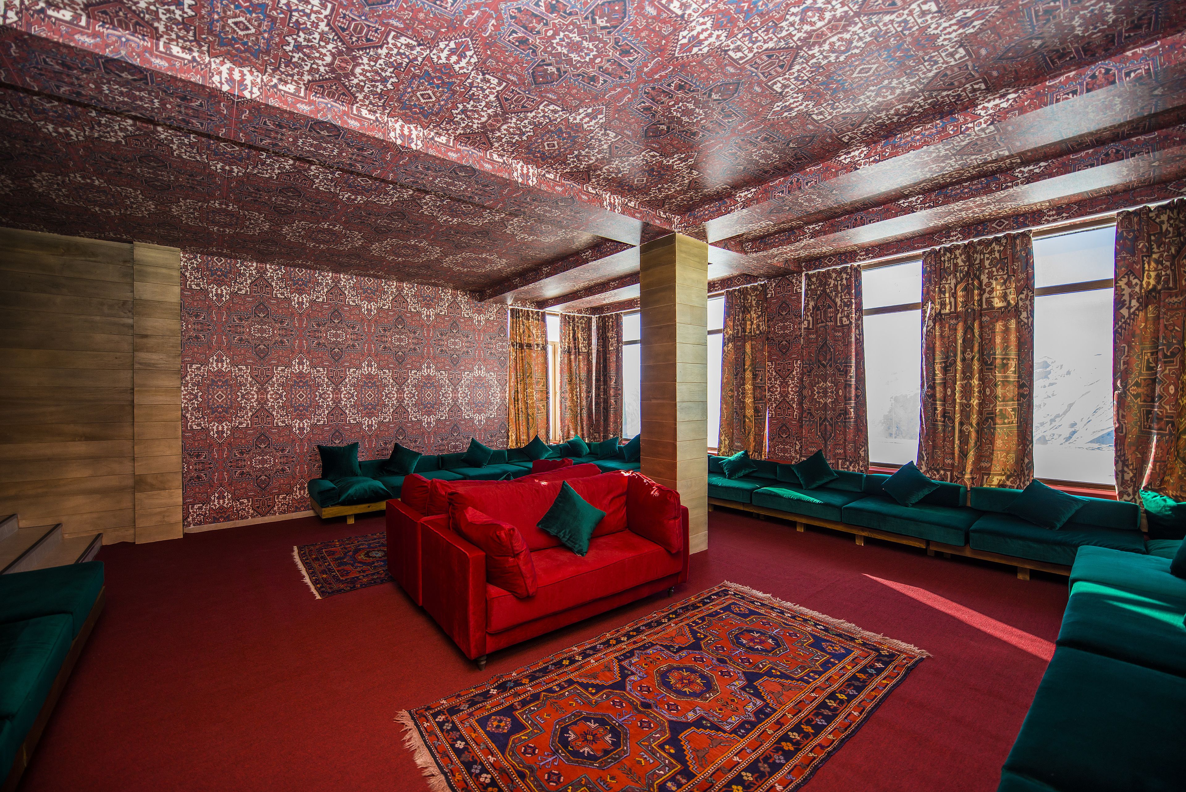 A room with a red sofa, teal cushions, and a patterned carpet.