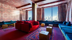Una habitación con un sofá rojo, algunos sofás azules y un ventanal con vistas a la montaña.