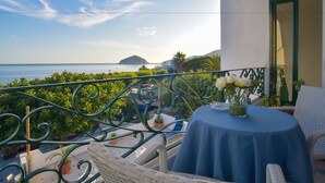 A balcony with a view of the sea, a table with a blue tablecloth, and white flowers. - Hotel Maronti (Barano d'Ischia)