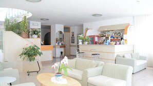 A modern hotel lobby with a bar area, seating arrangements, and potted plants. - Hotel Maronti (Barano d'Ischia)