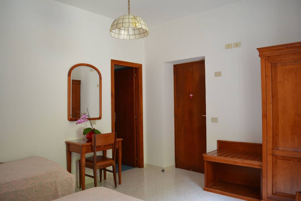 A room with a wooden desk, chair, and a mirror. There is a wooden bench and a door in the room.