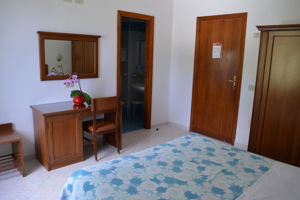A bedroom with a bed, a desk, a chair, a mirror, and two doors.