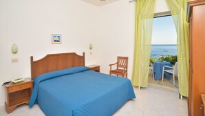 A bedroom with a bed, bedside table, chair, and a view of the sea through curtains. - Hotel Maronti (Barano d'Ischia)