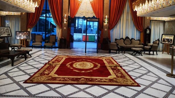 A grand lobby with a large ornate chandelier, red and gold drapery, and a patterned carpet. - Majliss Hotel (Rabat)