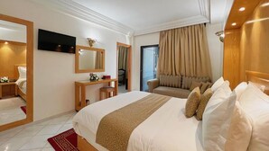 A hotel room with a large bed, a TV mounted on the wall, a desk with a chair, and a window with curtains. - Majliss Hotel (Rabat)