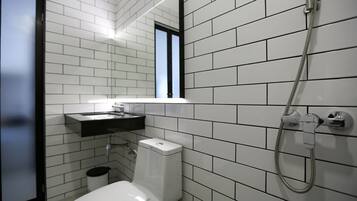 Un baño moderno con paredes de azulejos blancos, un inodoro blanco, un lavabo con encimera negra y una ducha con manguera.