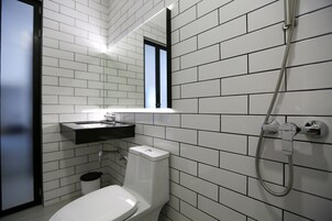 Un baño moderno con paredes de azulejos blancos, un inodoro blanco, un lavabo con encimera negra y una ducha con manguera.