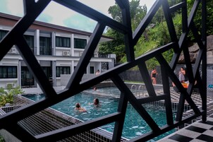 Una piscina con gente en el agua, rodeada por un edificio moderno con balcones y unidades de aire acondicionado.