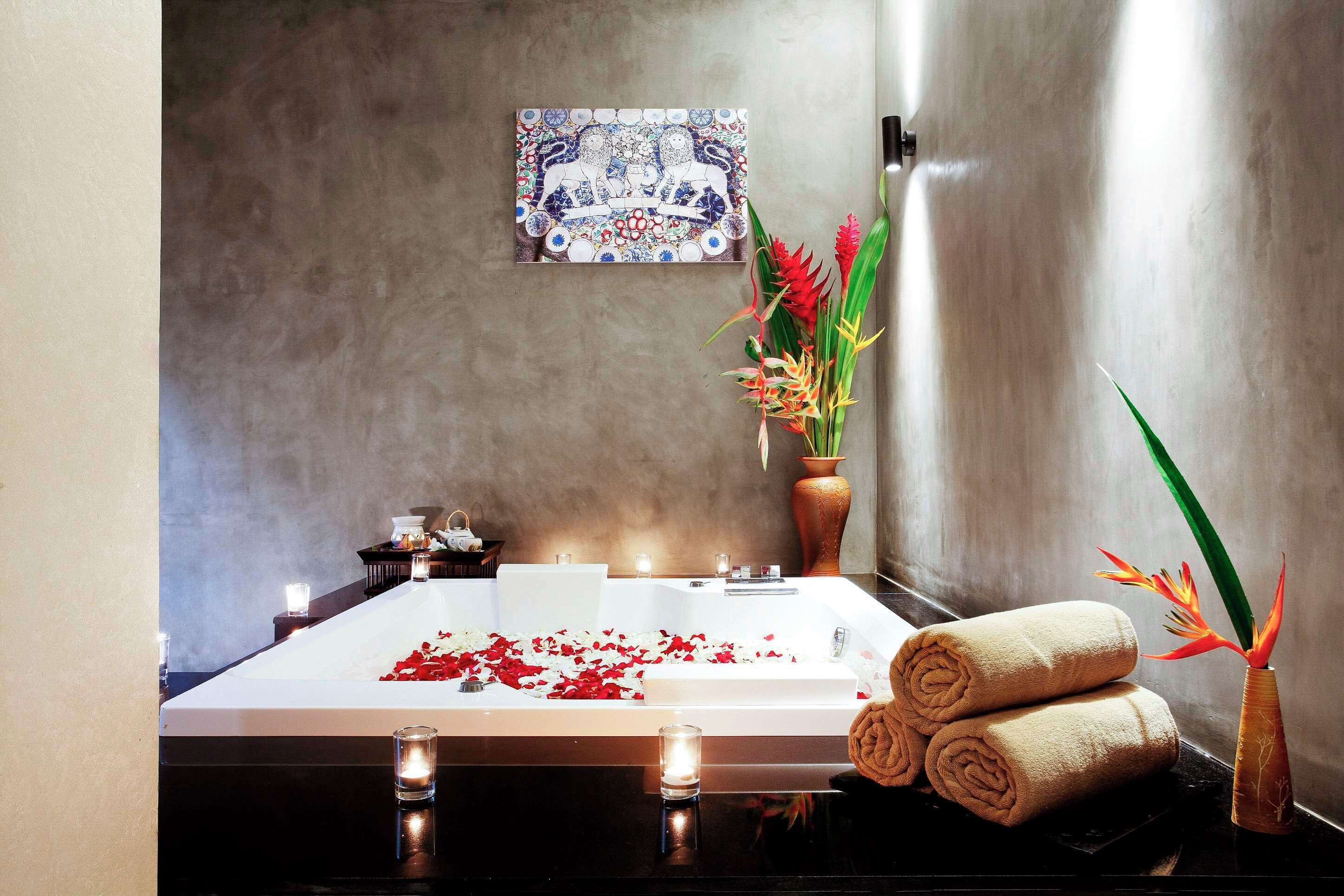 A modern bathroom with a large bathtub, decorative tiles, a vase with flowers, and rolled towels.