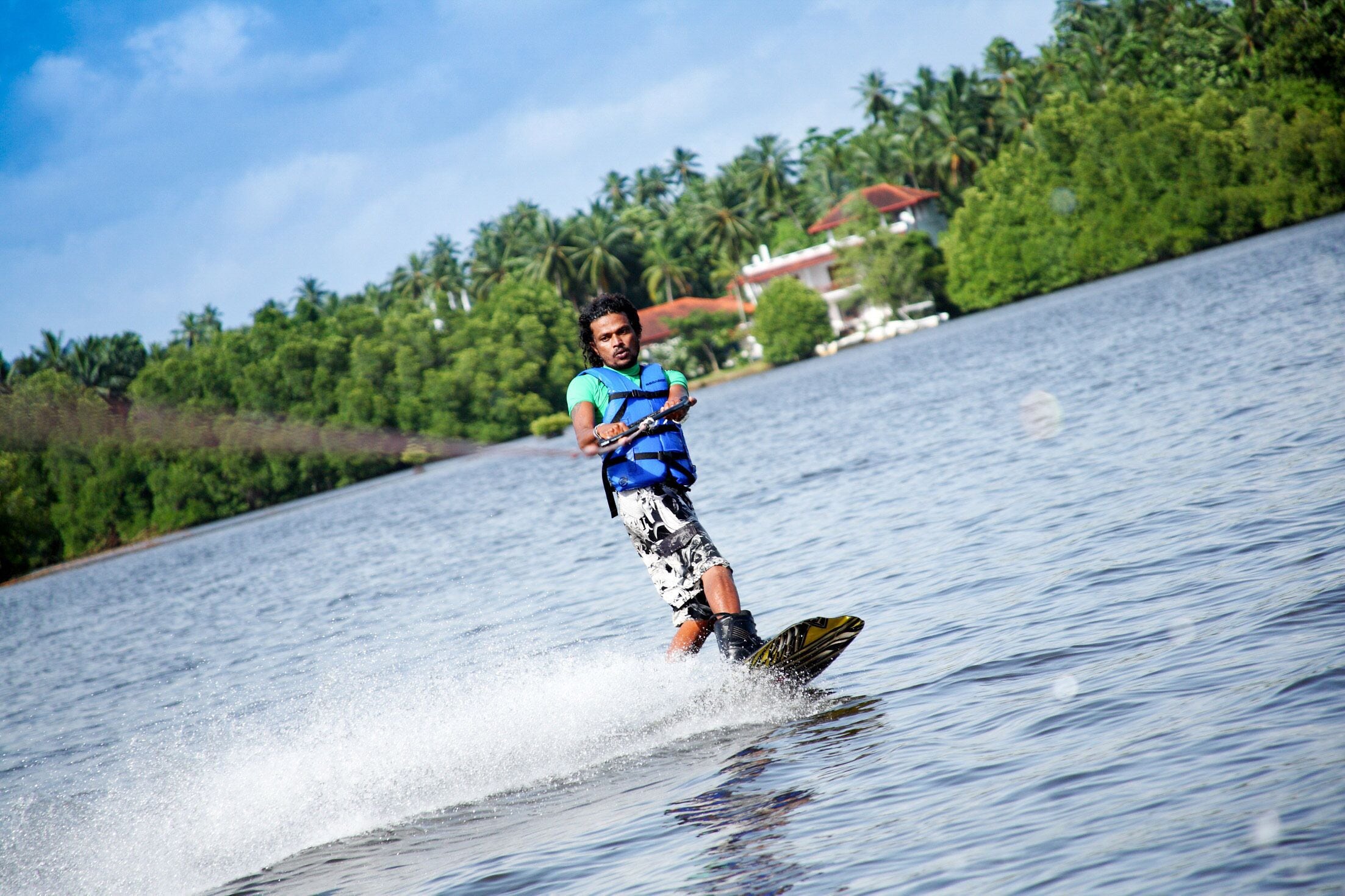 A person wakeboarding on a lake with a house and palm trees in the background.