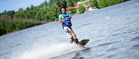 Une personne fait du wakeboard sur un lac, avec une maison et des palmiers en arrière-plan.