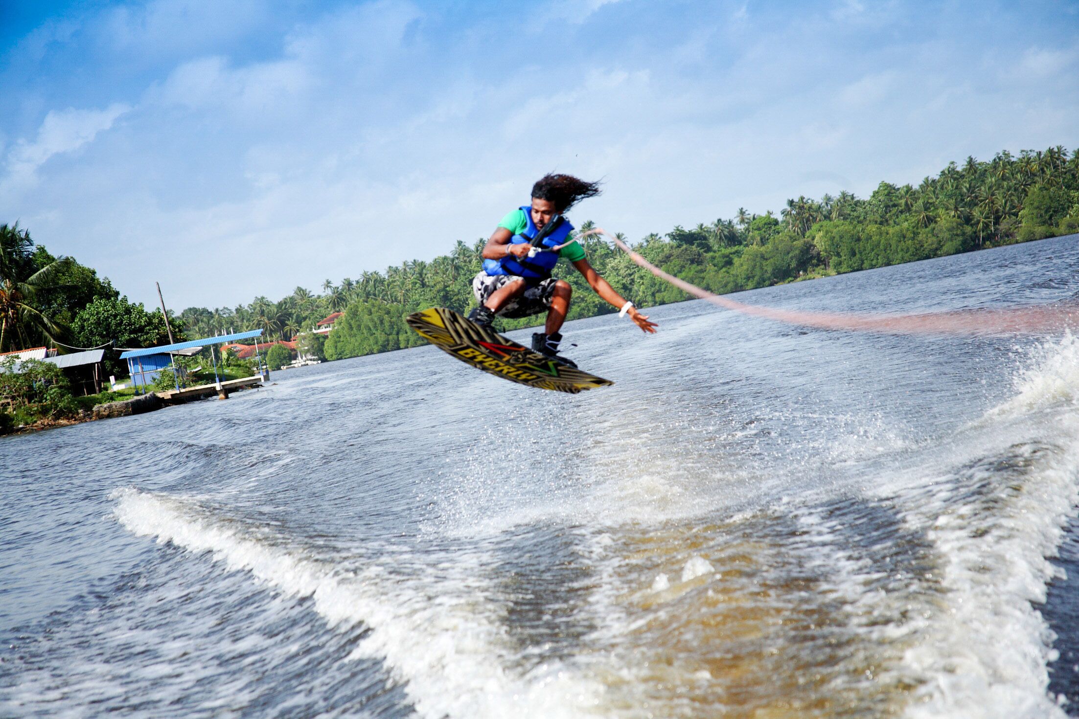 Eine Person treibt auf einem Riverboard einen Fluss, im Hintergrund Häuser und Bäume.