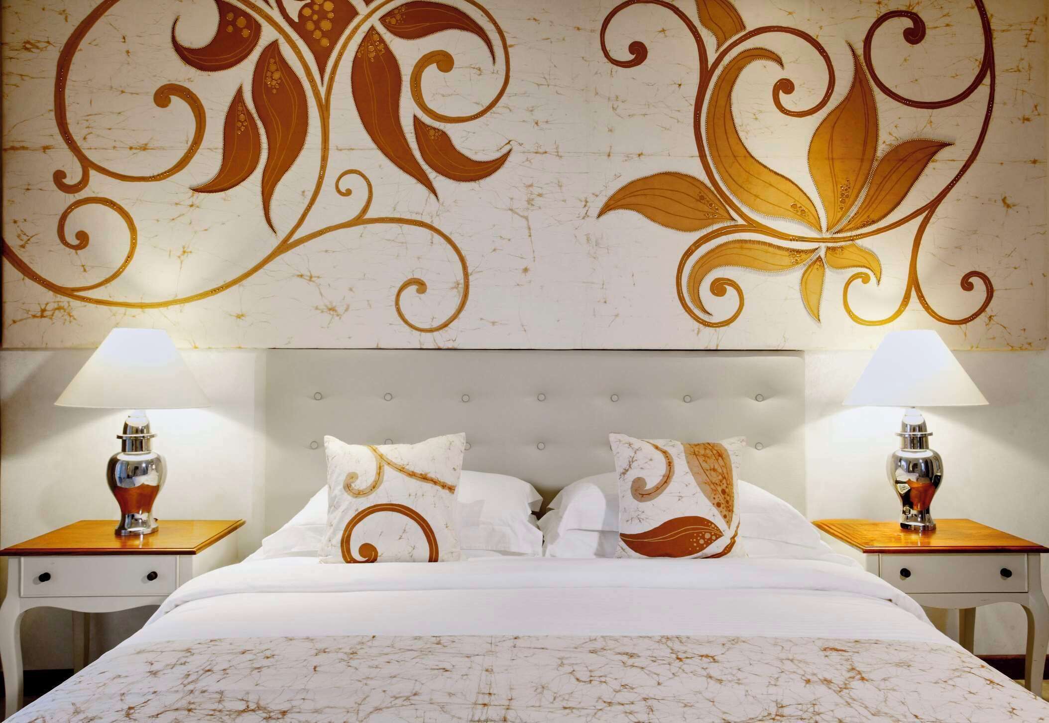 A hotel room with a large bed, two bedside tables with lamps, and a decorative wall design.