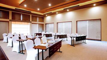 A conference room with multiple tables, white chairs, and large windows with blinds.