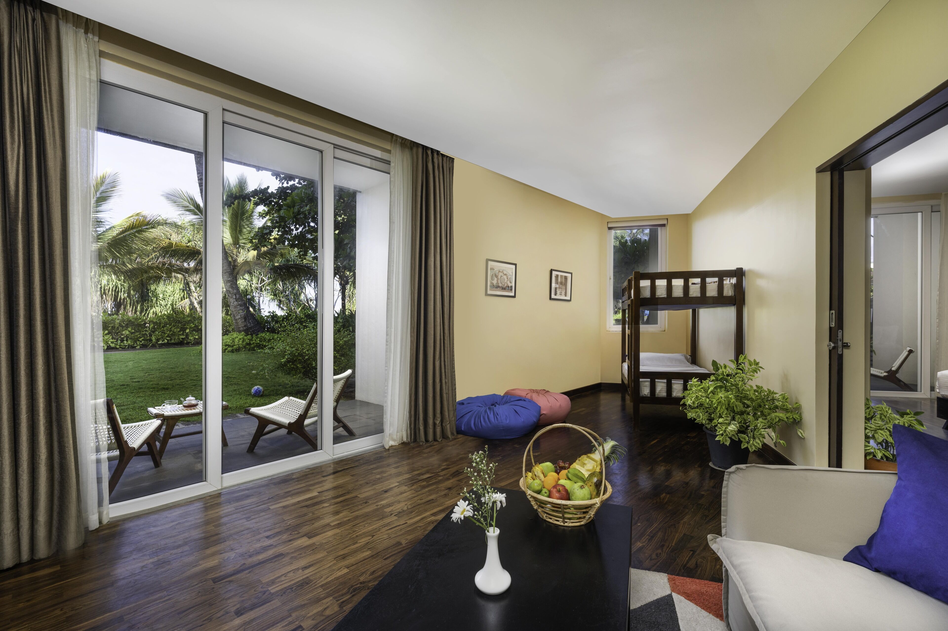 Una sala de estar moderna con un amplio ventanal corredera que da a un jardín, un sofá, una mesa de centro con un jarrón y una litera en la esquina.