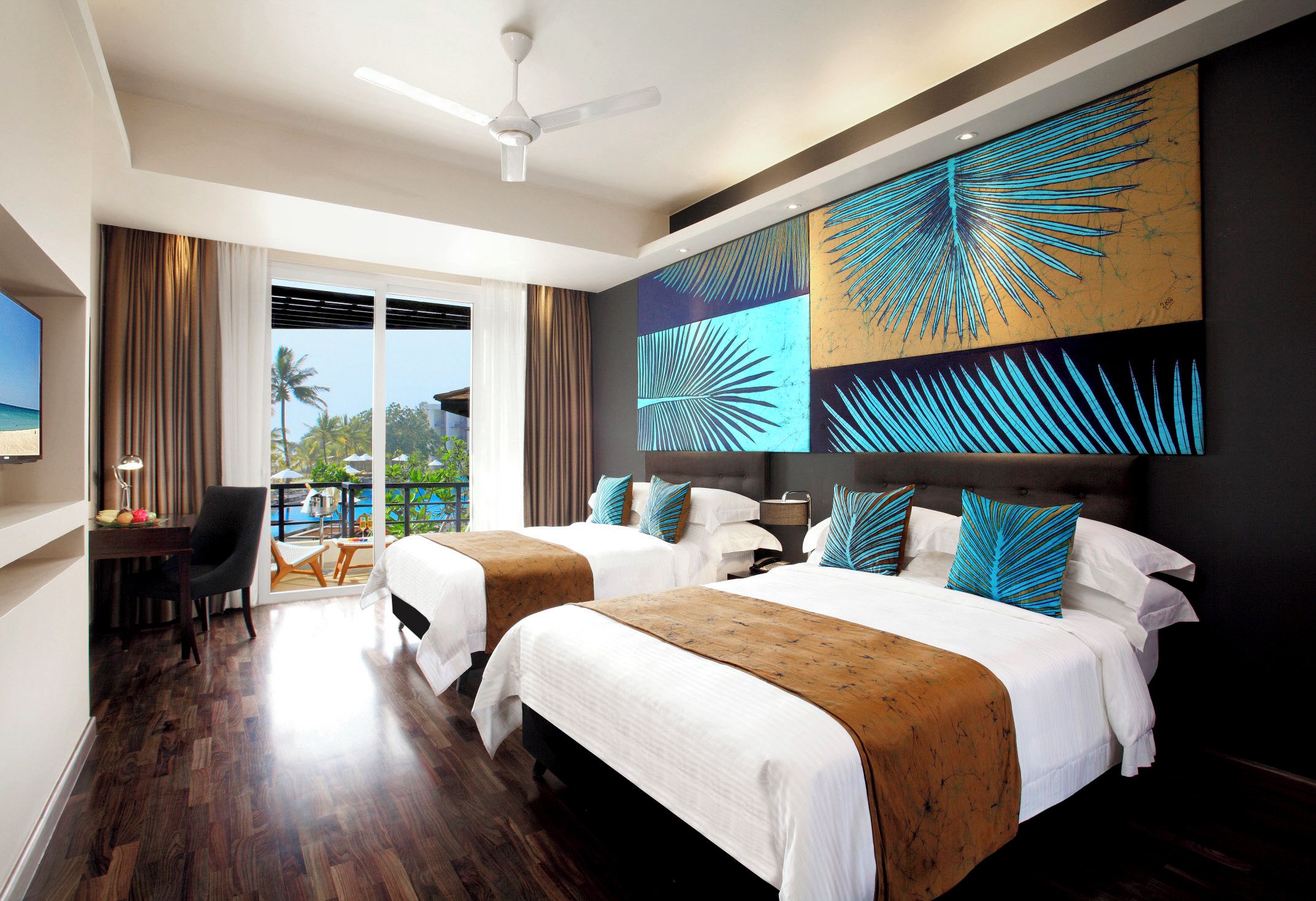 A hotel room with two beds, a desk, a chair, and a view of the beach.